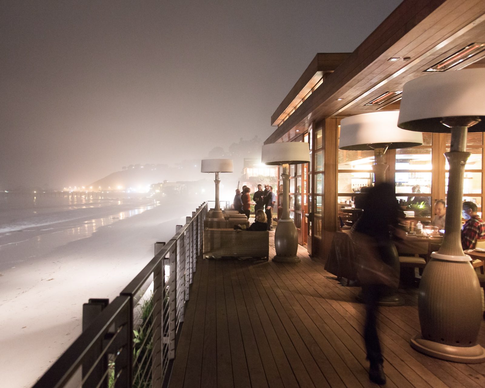 Guests gathered around Kindle heaters on a foggy oceanfront deck at night